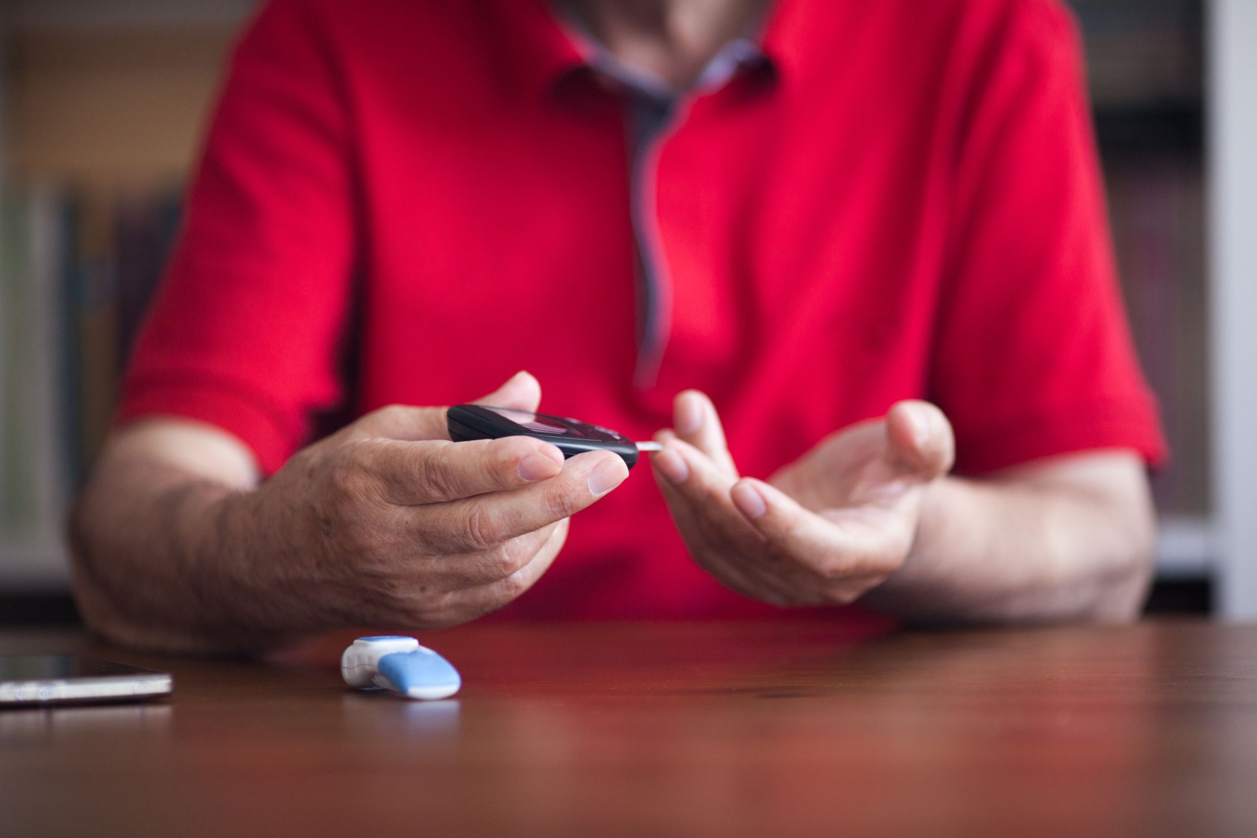 An older man in a red shirt tests his blood glucose level at home.