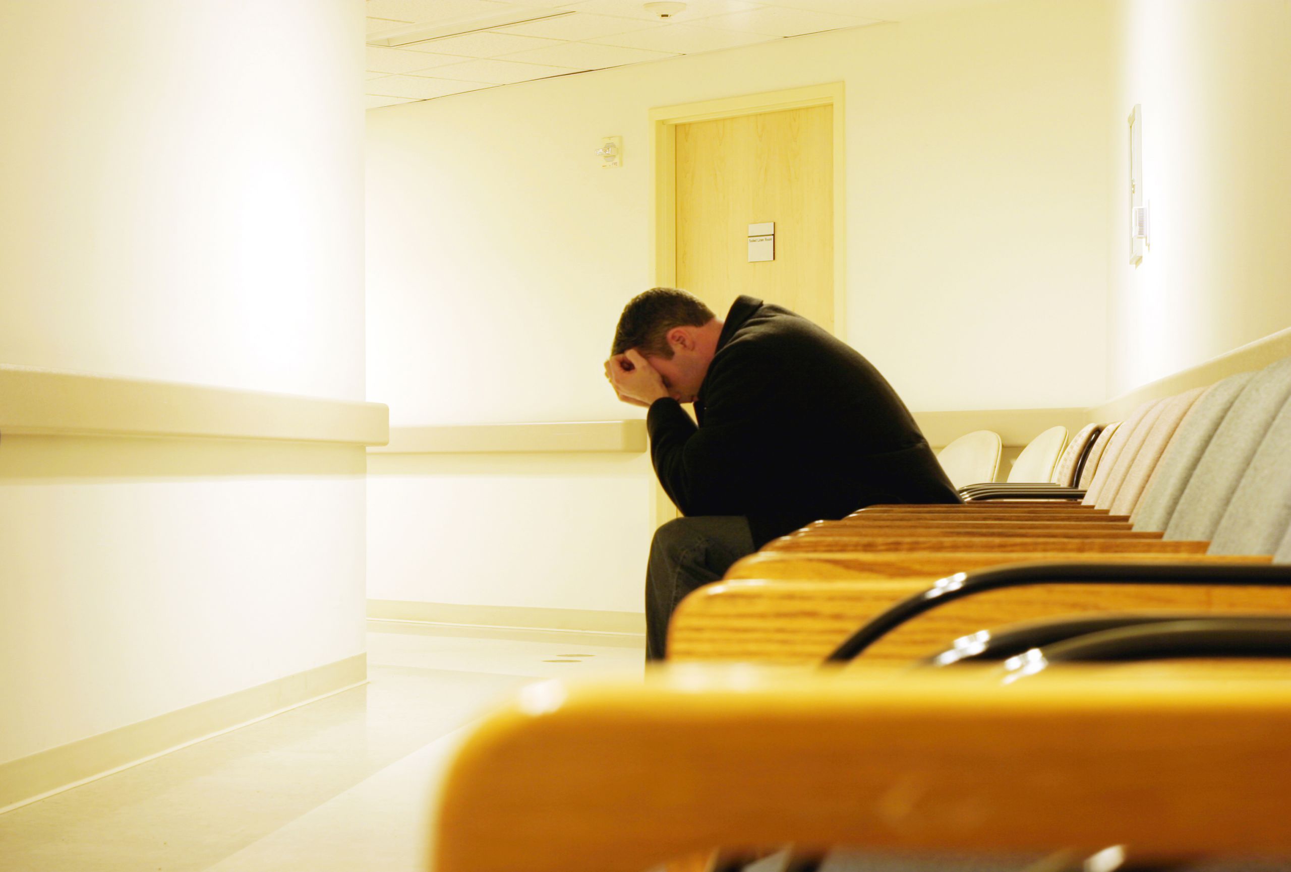 Image of a man waiting in a hospital corridor with his head in his hands.
